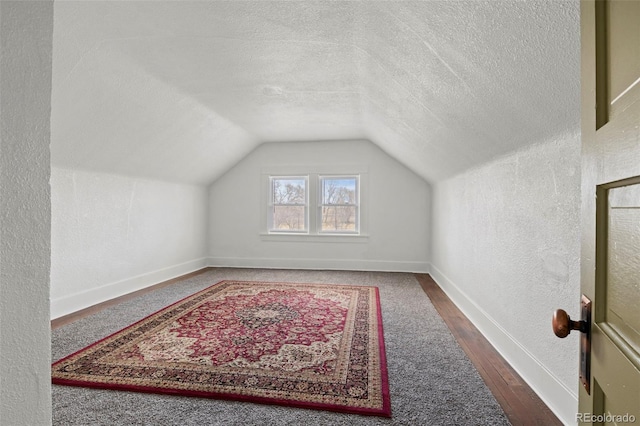 additional living space featuring lofted ceiling, a textured wall, baseboards, a textured ceiling, and wood finished floors