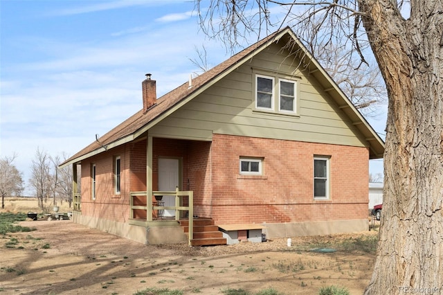 back of house with brick siding and a chimney