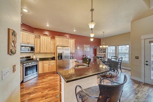 kitchen with sink, stainless steel appliances, hanging light fixtures, and light hardwood / wood-style flooring