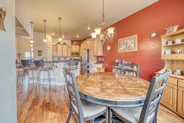 dining space with light hardwood / wood-style floors, sink, and an inviting chandelier