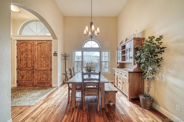 dining room with a towering ceiling, light wood-type flooring, and an inviting chandelier