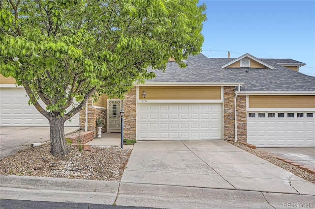 6727 W Yale Ave, Lakewood, CO 80227 - view of front of house with a shingled roof, stone siding, driveway, and a garage