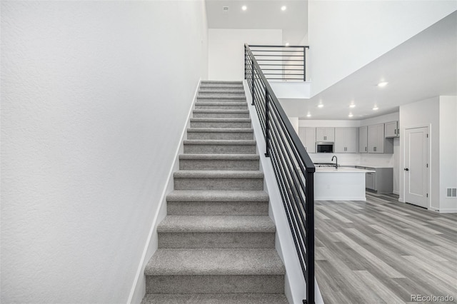 stairway with recessed lighting, baseboards, visible vents, a towering ceiling, and wood finished floors