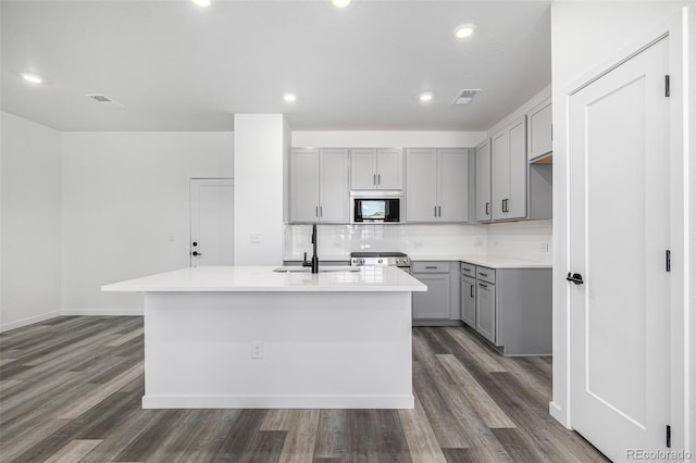 kitchen featuring built in microwave, visible vents, a sink, a center island with sink, and gray cabinets