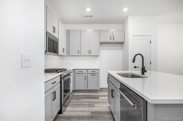 kitchen featuring appliances with stainless steel finishes, visible vents, a sink, an island with sink, and gray cabinets