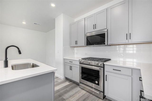 kitchen with a sink, stainless steel appliances, light wood-type flooring, backsplash, and light countertops