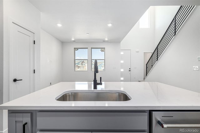 kitchen featuring dishwasher, gray cabinets, light stone countertops, and a sink