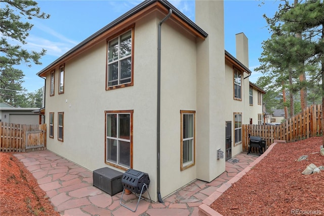 back of house with stucco siding, a patio area, fence, and a chimney