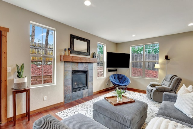 living area featuring a wealth of natural light, baseboards, wood finished floors, and a tiled fireplace