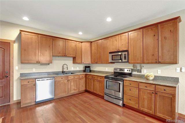 kitchen featuring recessed lighting, appliances with stainless steel finishes, light wood-style floors, brown cabinetry, and a sink