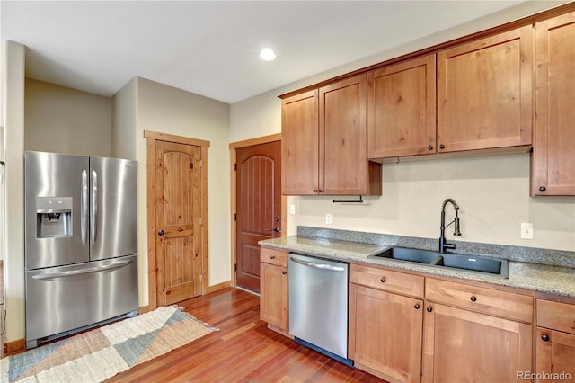 kitchen featuring a sink, light stone counters, stainless steel appliances, light wood-style floors, and baseboards