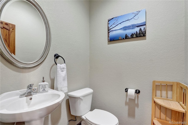 bathroom featuring toilet, a textured wall, and a sink