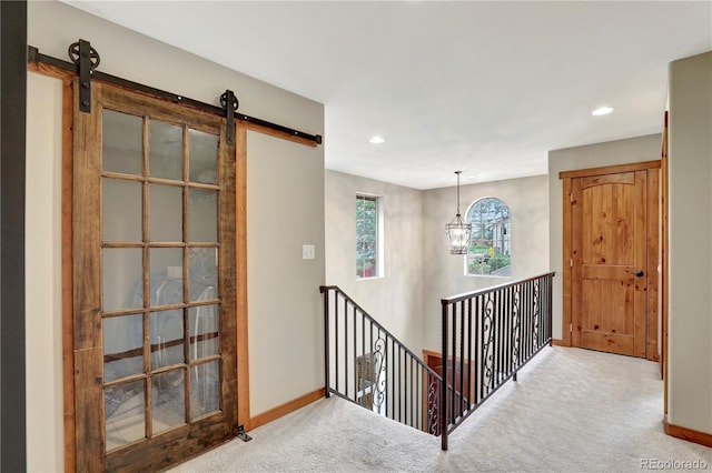 hall featuring a barn door, carpet flooring, and baseboards