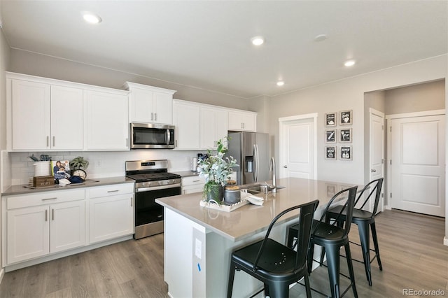 kitchen with a kitchen bar, appliances with stainless steel finishes, tasteful backsplash, a center island with sink, and white cabinets