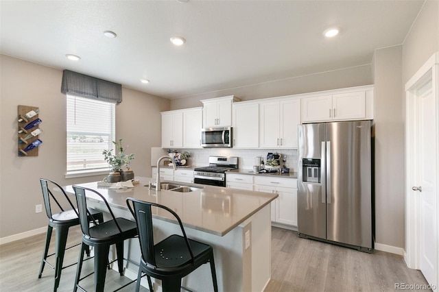 kitchen with backsplash, a kitchen island with sink, white cabinets, sink, and stainless steel appliances