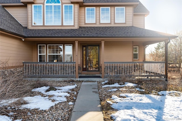 snow covered property entrance featuring a porch and a shingled roof