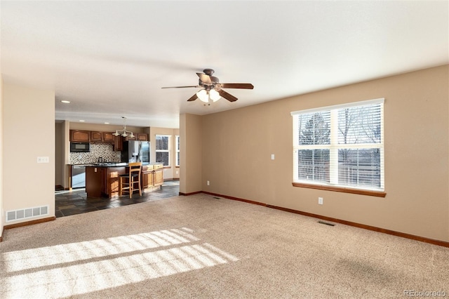 unfurnished living room featuring visible vents, dark carpet, baseboards, and ceiling fan with notable chandelier