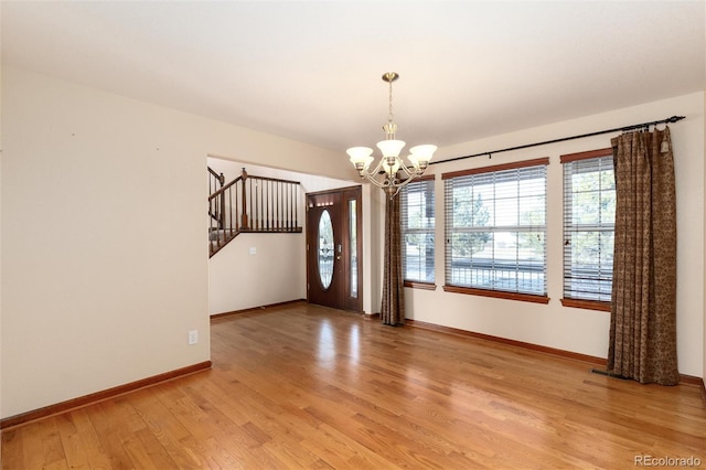 entrance foyer featuring baseboards, a notable chandelier, light wood finished floors, and stairs