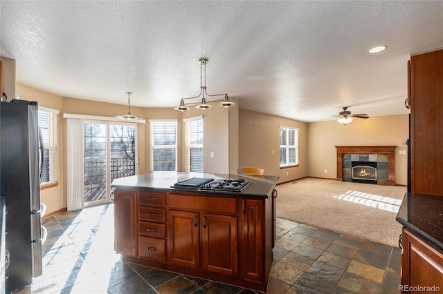 kitchen with a fireplace, stone tile floors, black gas cooktop, dark countertops, and freestanding refrigerator