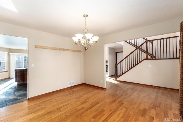 empty room featuring light wood-style floors, visible vents, stairway, and baseboards