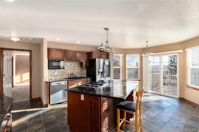 kitchen featuring stone tile floors, a sink, baseboards, appliances with stainless steel finishes, and decorative backsplash