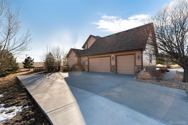 view of side of home featuring driveway, stone siding, a garage, and roof with shingles