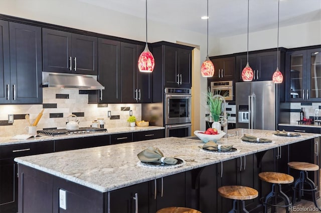24322 E Mineral Dr, Aurora, CO 80016 - kitchen with stainless steel appliances, under cabinet range hood, decorative backsplash, glass insert cabinets, and a kitchen island