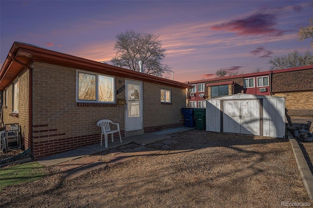 back house at dusk with a patio area and a storage unit