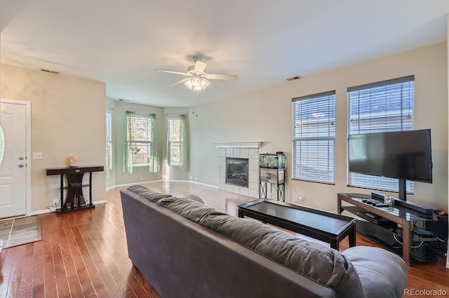 living room featuring ceiling fan, dark hardwood / wood-style floors, and a tiled fireplace