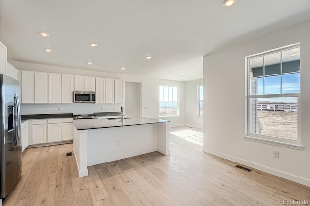 kitchen featuring sink, light hardwood / wood-style flooring, stainless steel appliances, an island with sink, and white cabinets