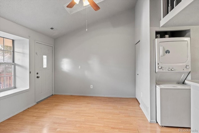 entrance foyer featuring ceiling fan, light hardwood / wood-style flooring, a textured ceiling, lofted ceiling, and stacked washer and clothes dryer