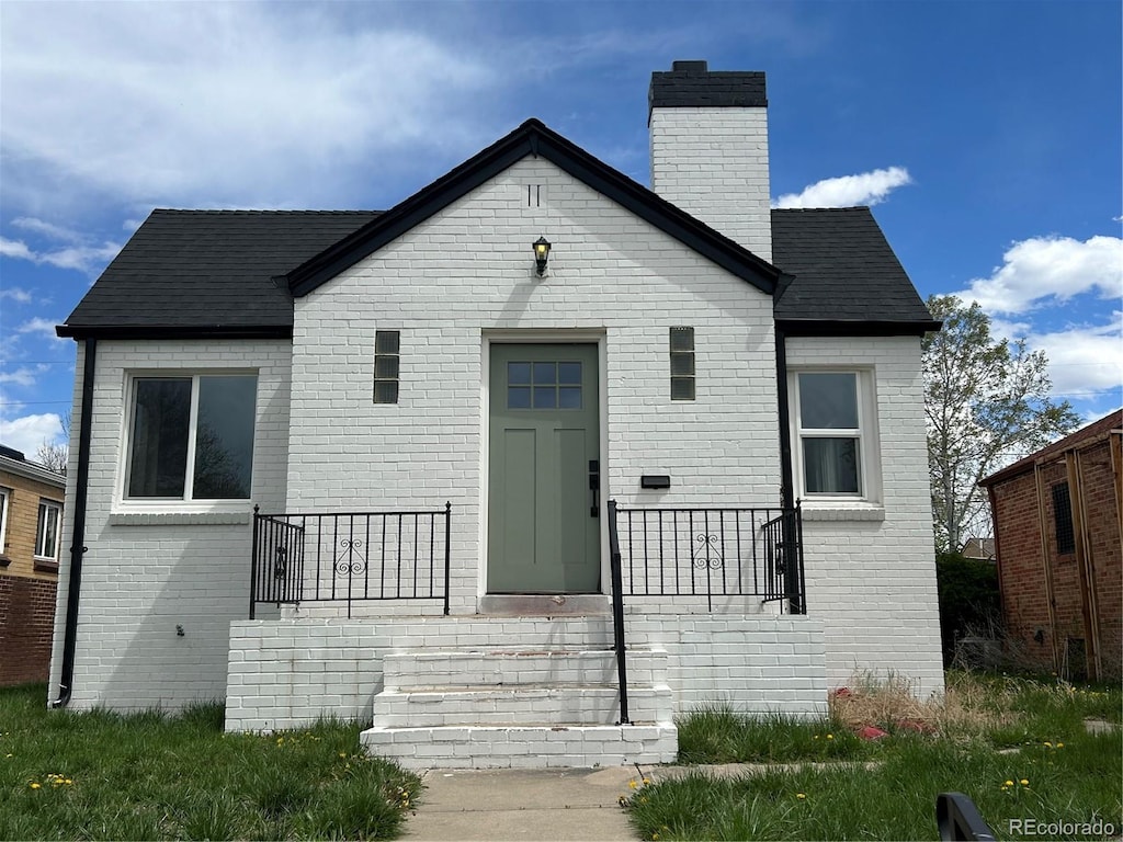 view of front of home featuring brick siding, a shingled roof, and a chimney