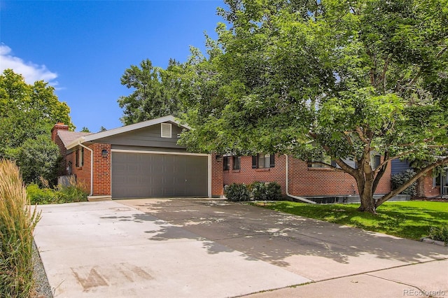 7036 Robb St, Arvada, CO 80004 - view of property hidden behind natural elements featuring brick siding, an attached garage, concrete driveway, and a chimney