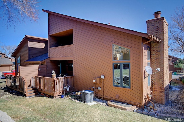 rear view of house with a chimney, central AC, a deck, and a lawn