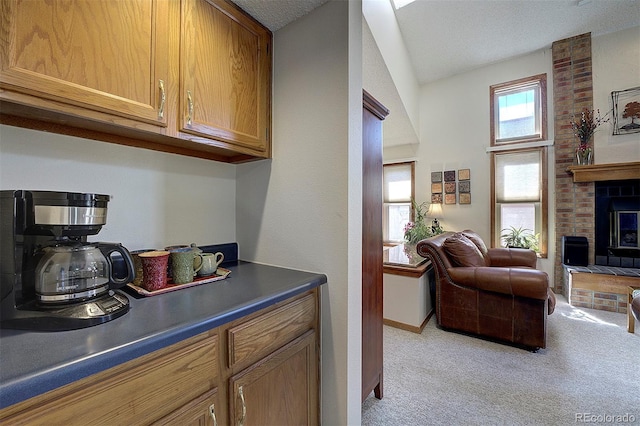 kitchen featuring brown cabinetry, light colored carpet, dark countertops, open floor plan, and a brick fireplace