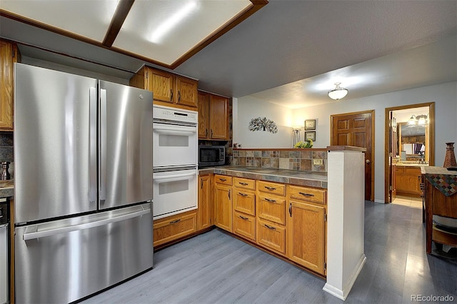 kitchen with white double oven, decorative backsplash, freestanding refrigerator, black microwave, and a peninsula