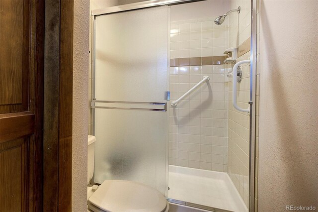 full bathroom with a textured wall, a shower stall, and toilet