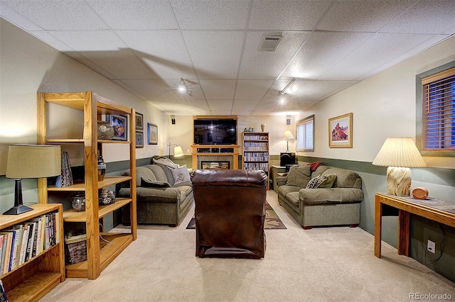 carpeted living area featuring visible vents, a drop ceiling, and a glass covered fireplace