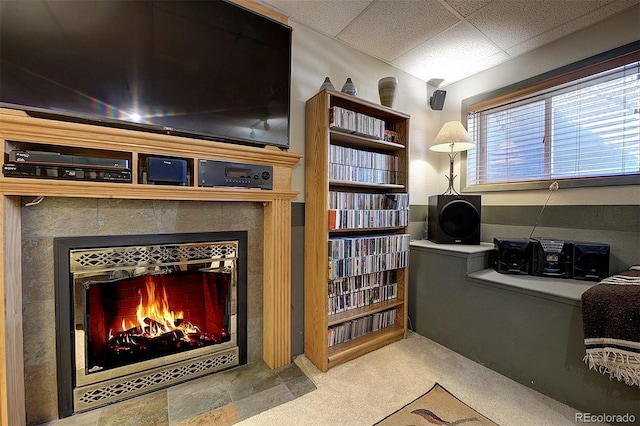 interior space with a drop ceiling, carpet, and a tile fireplace