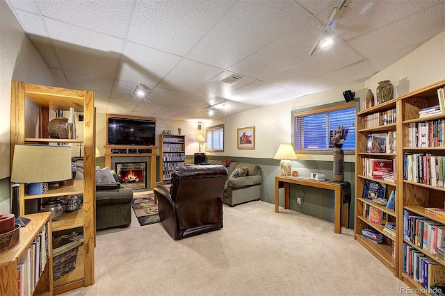 living room featuring carpet, visible vents, a drop ceiling, and a lit fireplace