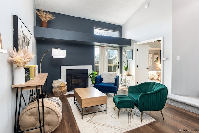 living area with a fireplace with flush hearth, high vaulted ceiling, a textured ceiling, and wood finished floors