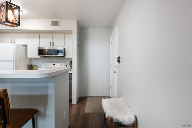 kitchen featuring dark wood-type flooring, a breakfast bar, light countertops, freestanding refrigerator, and stainless steel microwave