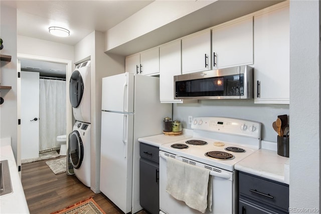 kitchen with white appliances, dark wood-style flooring, white cabinets, stacked washer / drying machine, and light countertops