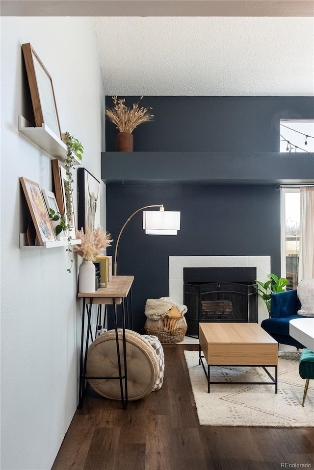 living area featuring a textured ceiling, a tiled fireplace, and wood finished floors