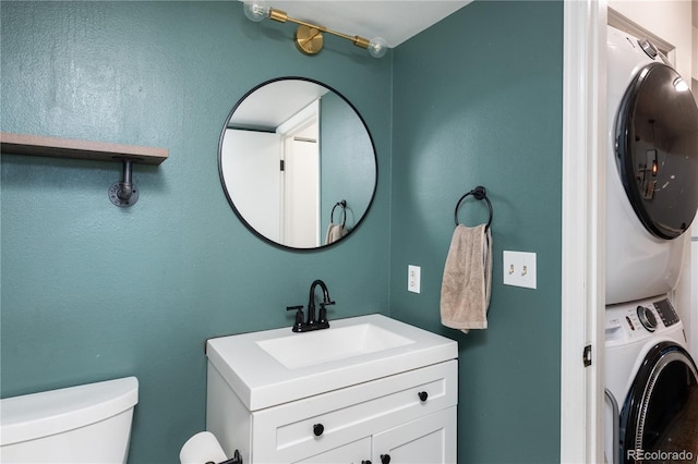 bathroom featuring stacked washer / drying machine, vanity, and toilet