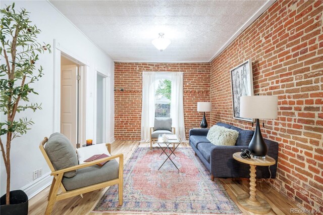 sitting room featuring wood finished floors, crown molding, a textured ceiling, brick wall, and baseboards