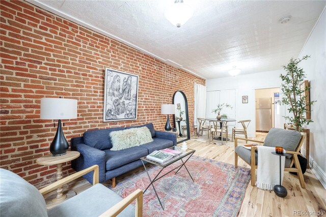 living room featuring wood finished floors, brick wall, baseboards, and a textured ceiling