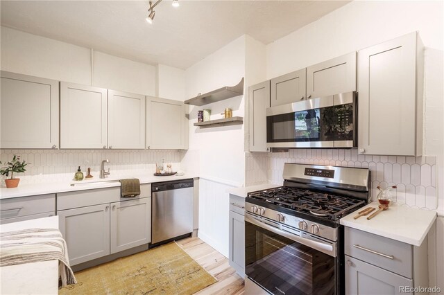kitchen featuring stainless steel appliances, gray cabinets, a sink, open shelves, and light countertops