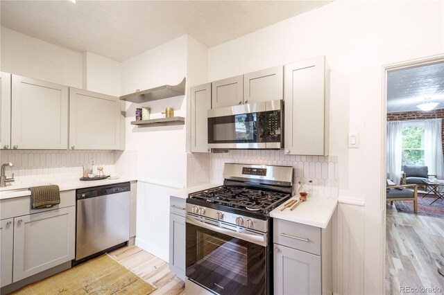 kitchen featuring stainless steel appliances, gray cabinets, light wood-type flooring, open shelves, and light countertops