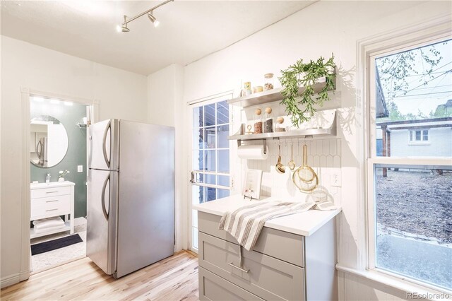 kitchen with freestanding refrigerator, light wood finished floors, light countertops, open shelves, and track lighting